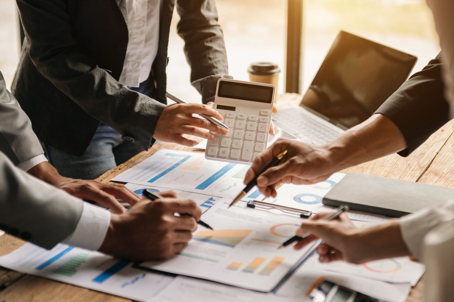 A team of people gather around a desk covered with financial documents showing the allocation of assets by asset classes.