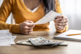 Close-up picture of the hands of a young woman checking shopping receipts in front of a stack of dollars