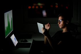 Young man looking at a tablet in front of a computer screen and laptop showing financial information