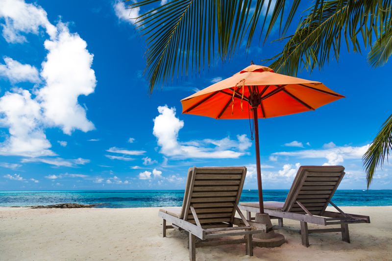 Beautiful beach background for summer travel with sun,coconut tree and beach wooden bed on sand with beautiful blue sea and blue sky. Summer mood sun beach background concept.