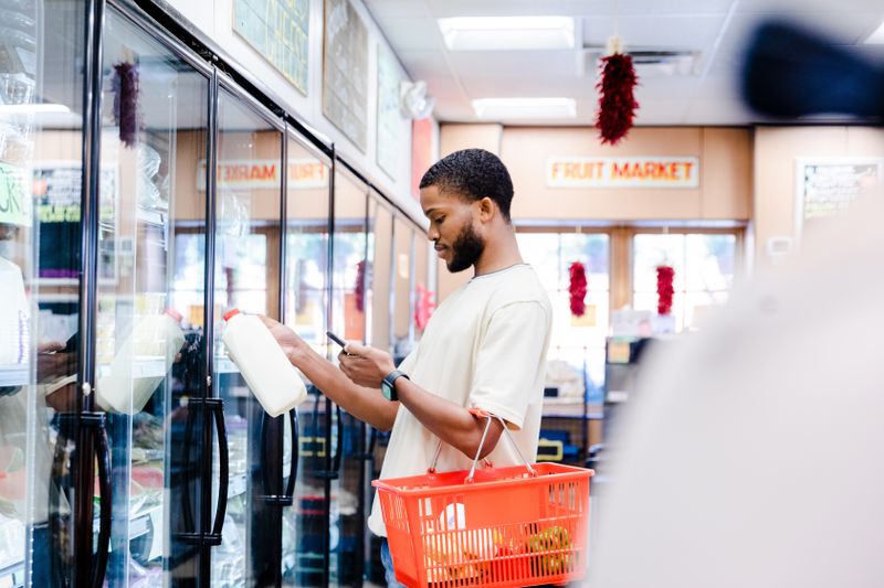 A young adult man checks a coupon app while grocery shopping.