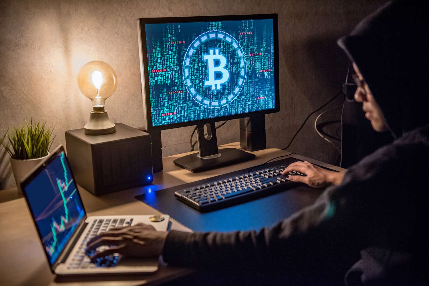 A hacker working on a desktop and laptop to hack bitcoin.