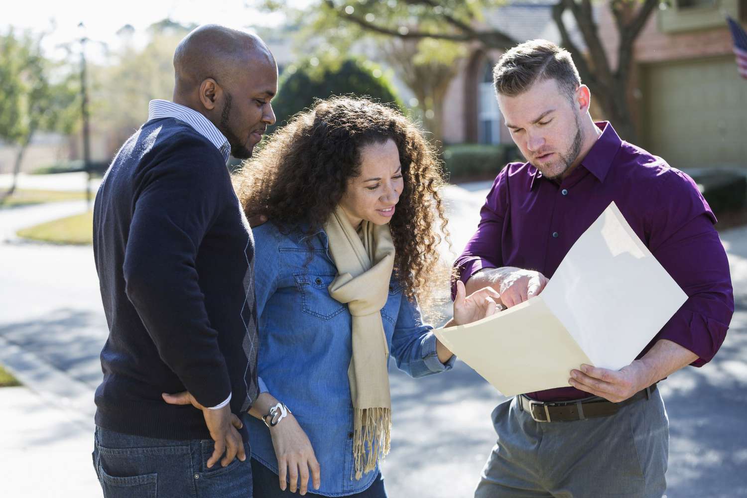 Two homeowner clients looking at a folder with a salesman on the street in a residential block.