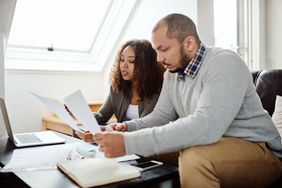 Young couple sitting on their sofa and looking together at mortgage documents and rates on a laptop