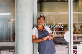 cafe owner stands in her restaurant using smartphone