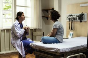 Female doctor talking to 25-year-old female patient in exam room