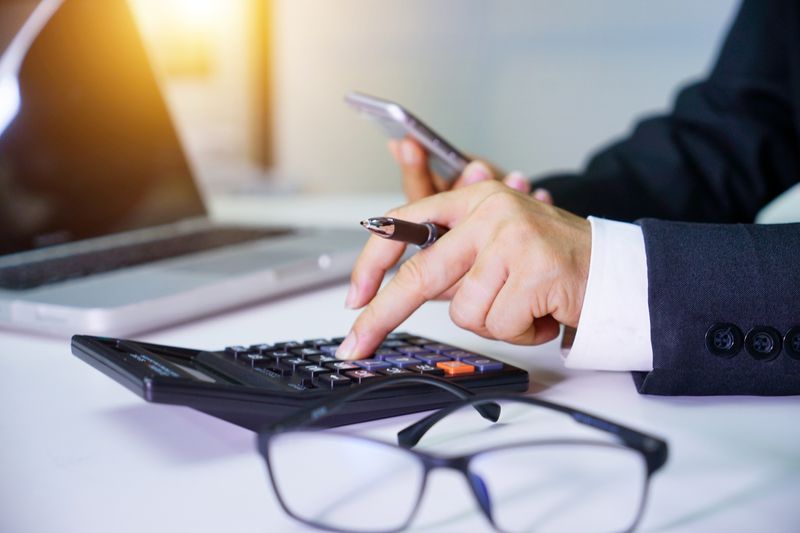 Someone in a suit using a calculator next to glasses