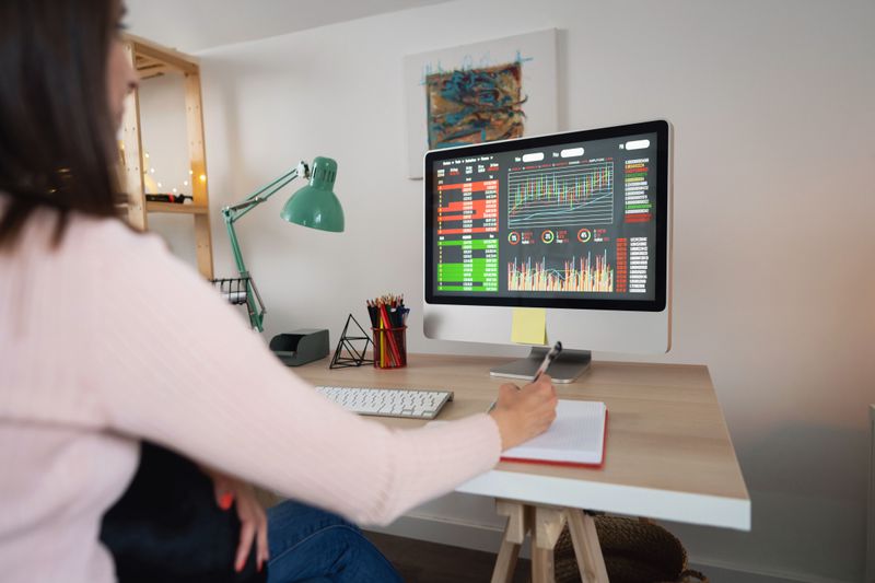 Woman looking at financial data on a monitor while writing in a note pad.