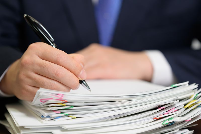 Business person holding a pen and signing a stack of paperwork 