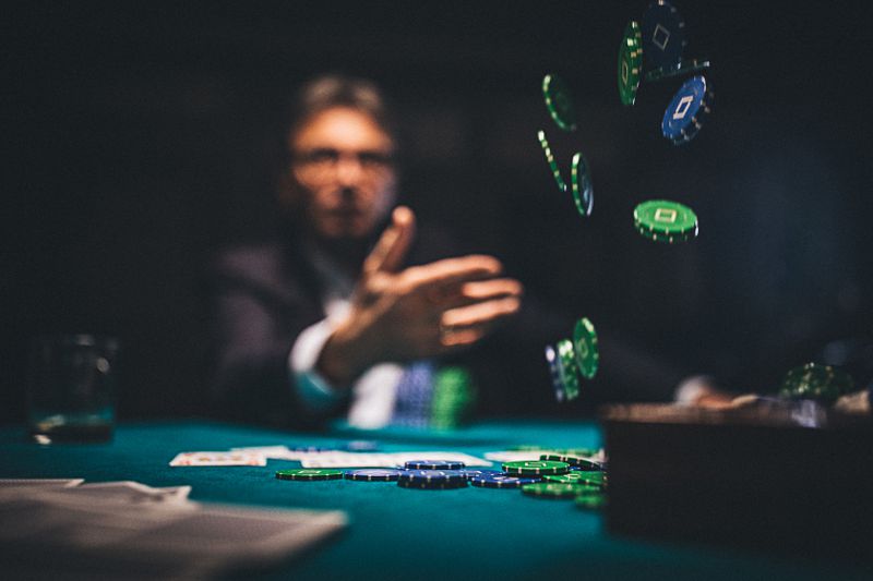 A person in the background in a dark casino throwing casino chips toward the center of the table.