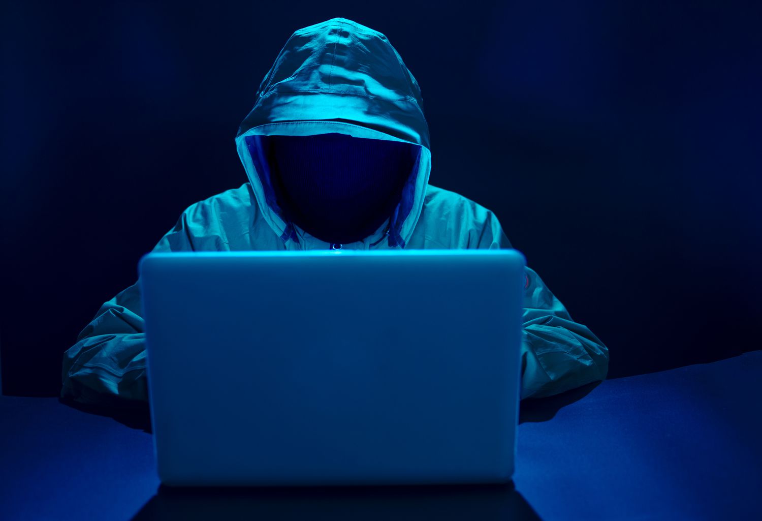 computer hacket in front of a laptop with their face concealed wearing a hood