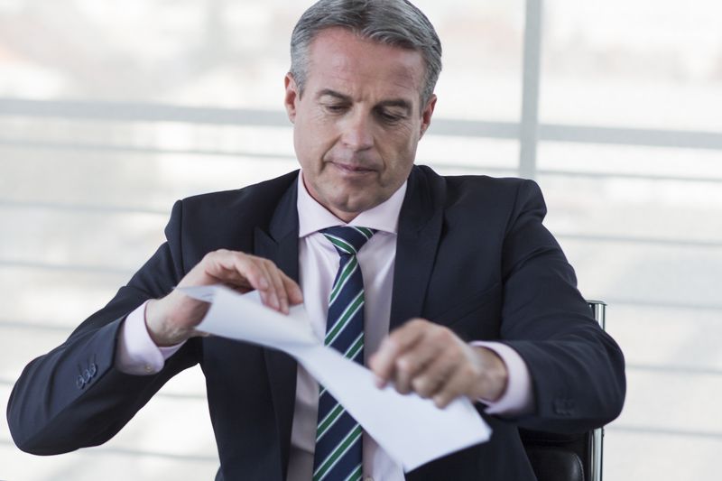 Senior banker sitting at his desk opening a deceased alert in his office