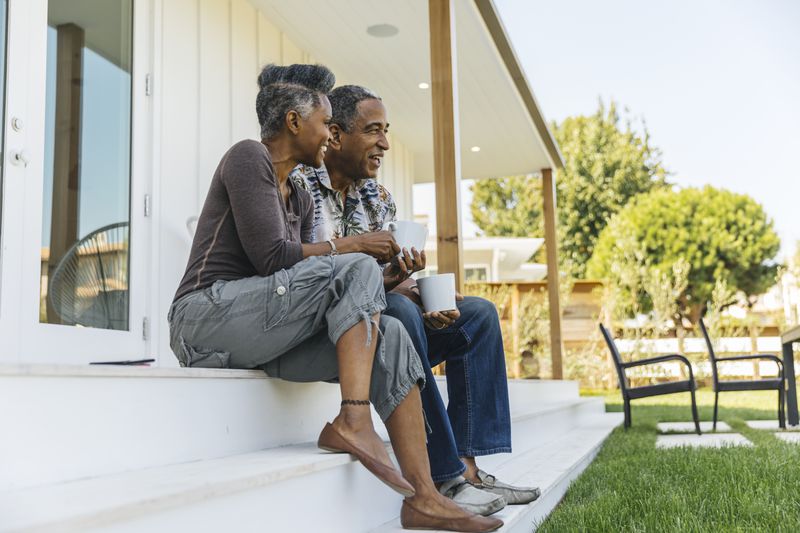 A man and a woman sip coffee while sitting on steps of front porch of house