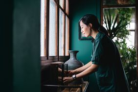 Young Asian woman decorating and arranging picture frames and home decorations over the cabinet at home. 