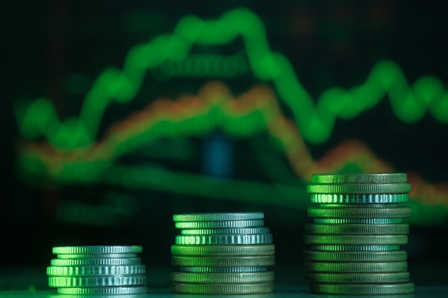Stack of coin on laptop against stock market charts on laptop screen.