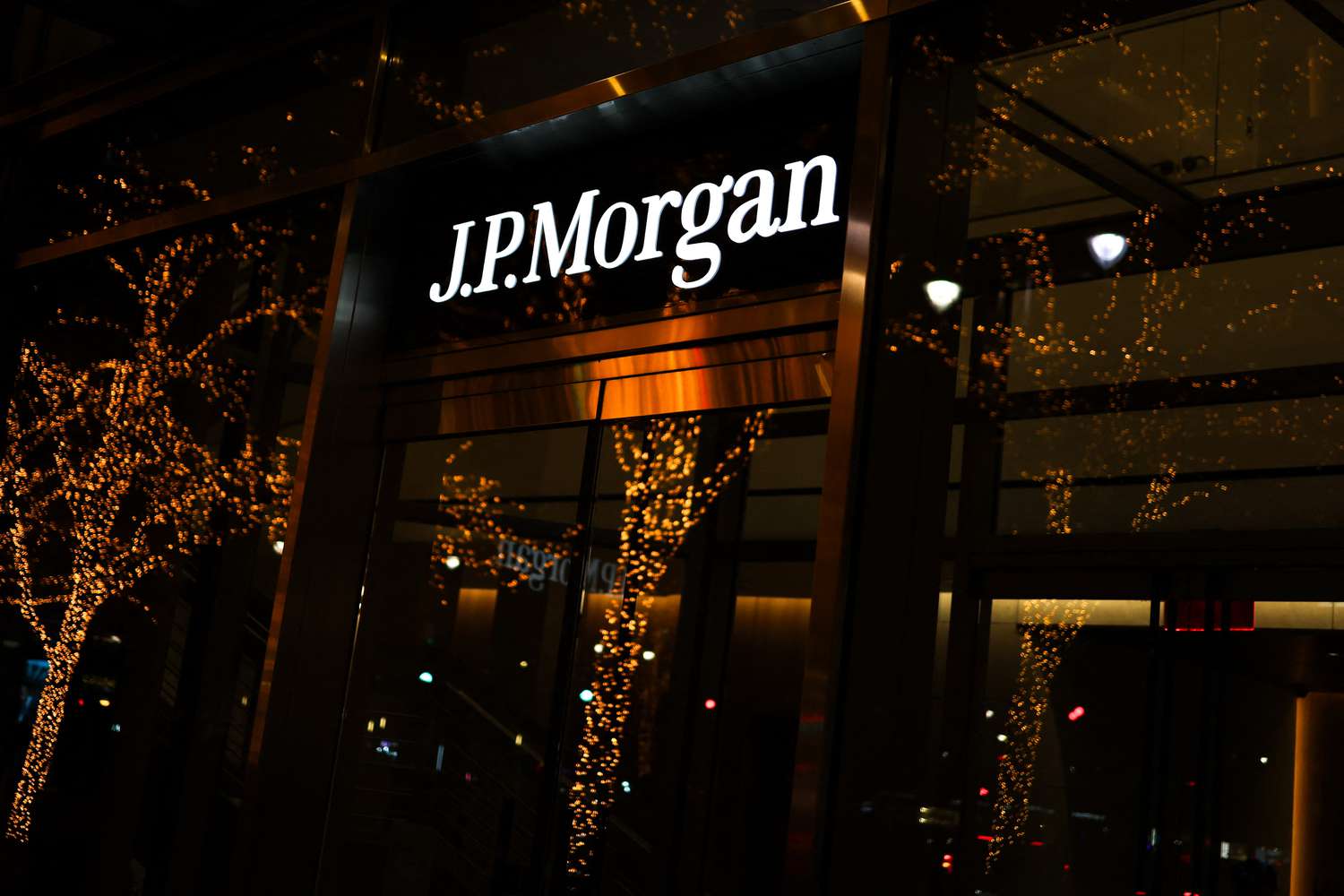 The J.P.Morgan sign is seen on the side of a building, as a tree with Christmas lights is seen outside.