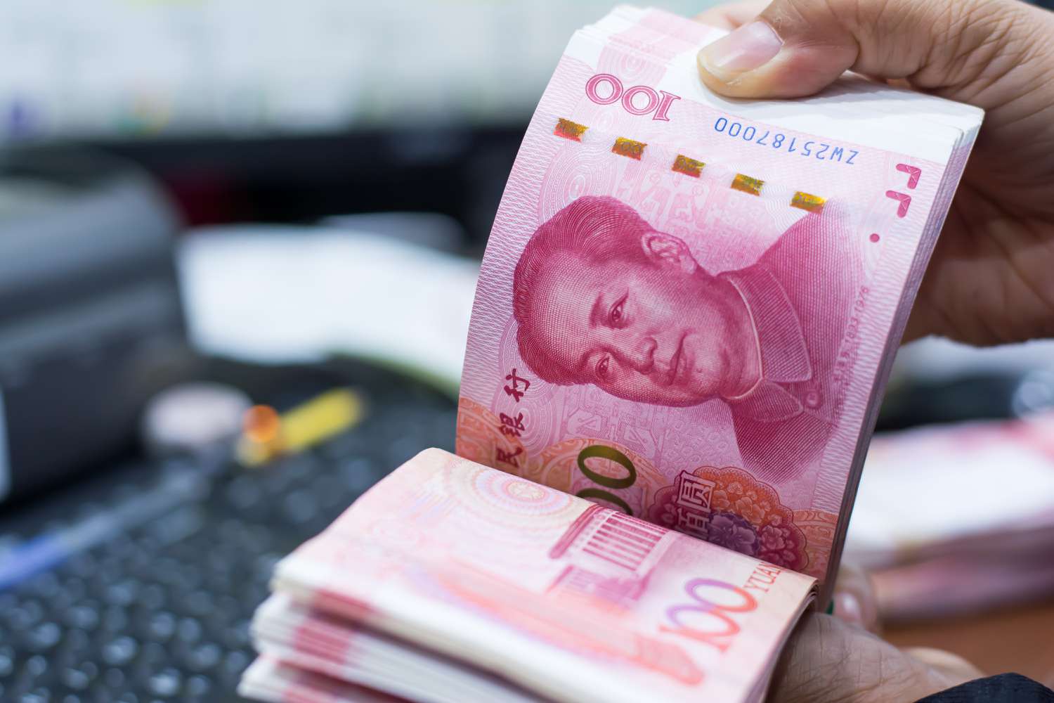 A person counting a stack of Chinese yuan bank notes.