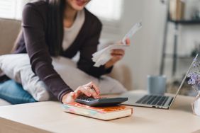 Close up of woman using calculator and holding receipts while managing finances at home