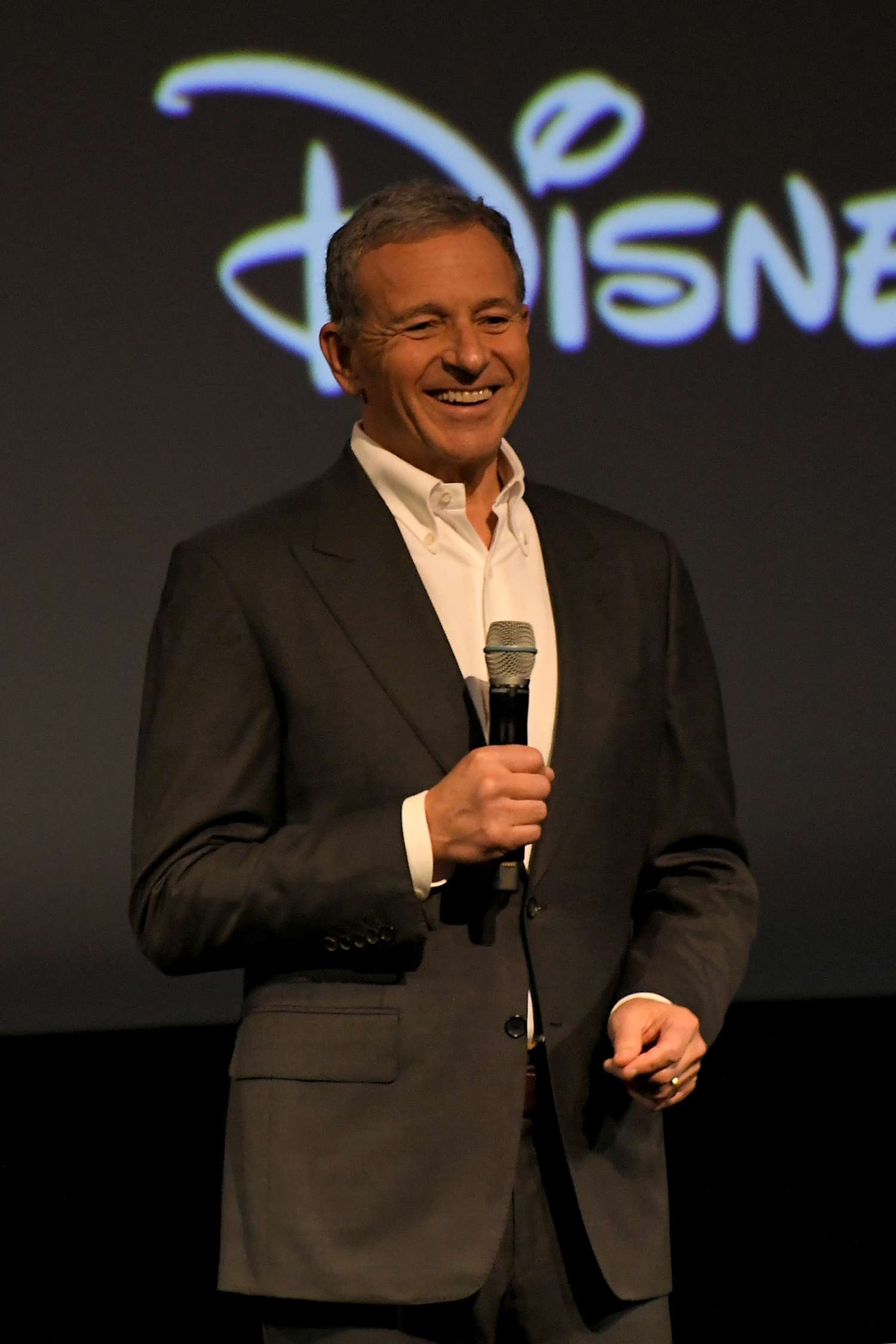 Bob Iger standing with a microphone in front of a partially-obscured Disney logo
