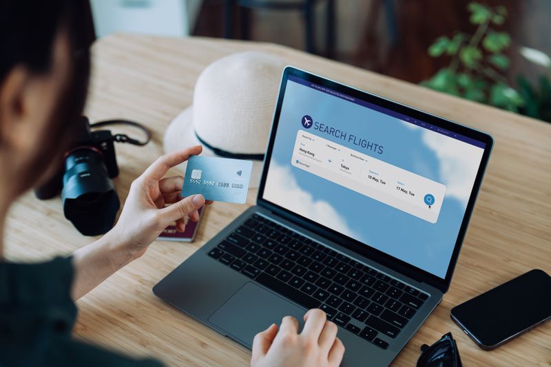 Person reviewing a flight searching website on a laptop while holding a credit card