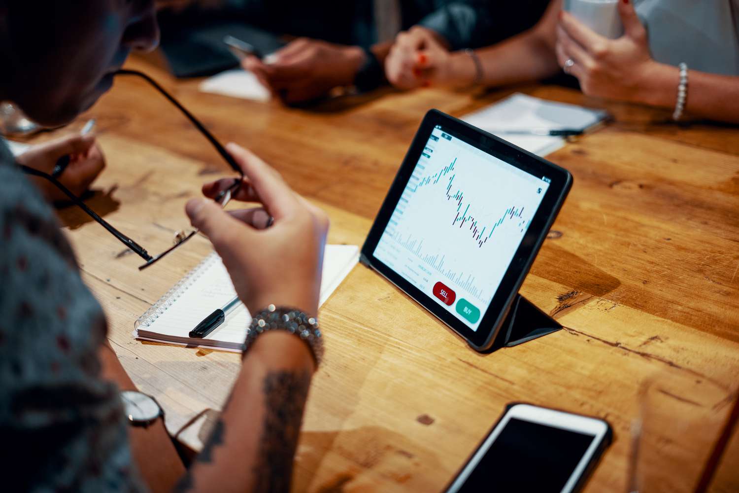 Mixed group of millennial aged friends discuss investing and cryptocurrency trading at a cafe. Depicts TradingView financial market chart.