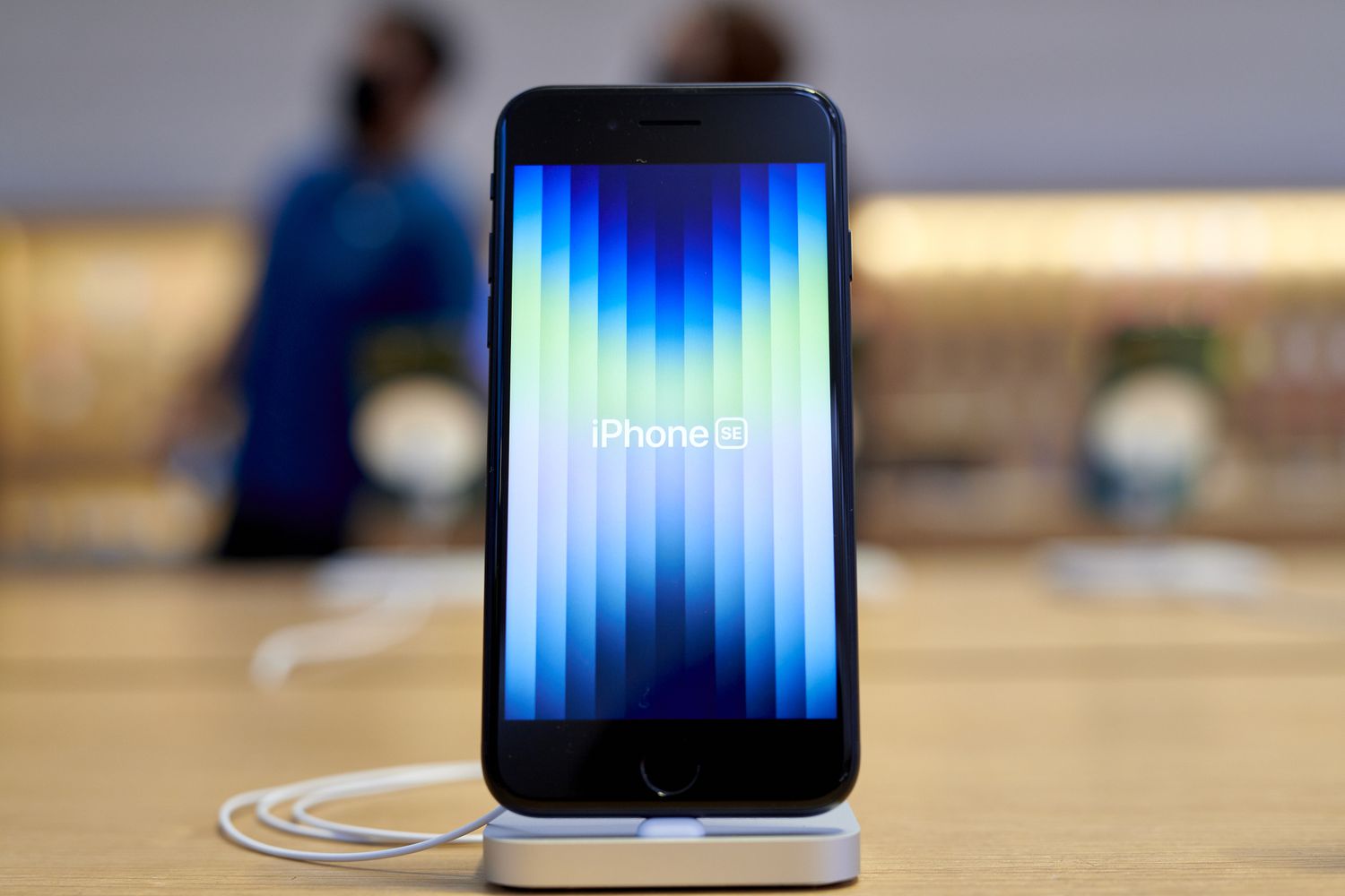 An iPhone SE with a light blue background sits on a table.