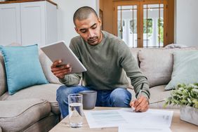 A person doing online banking on tablet while filling out papers.