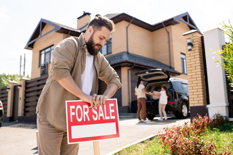 Man putting a For Sale sign up in front of a house