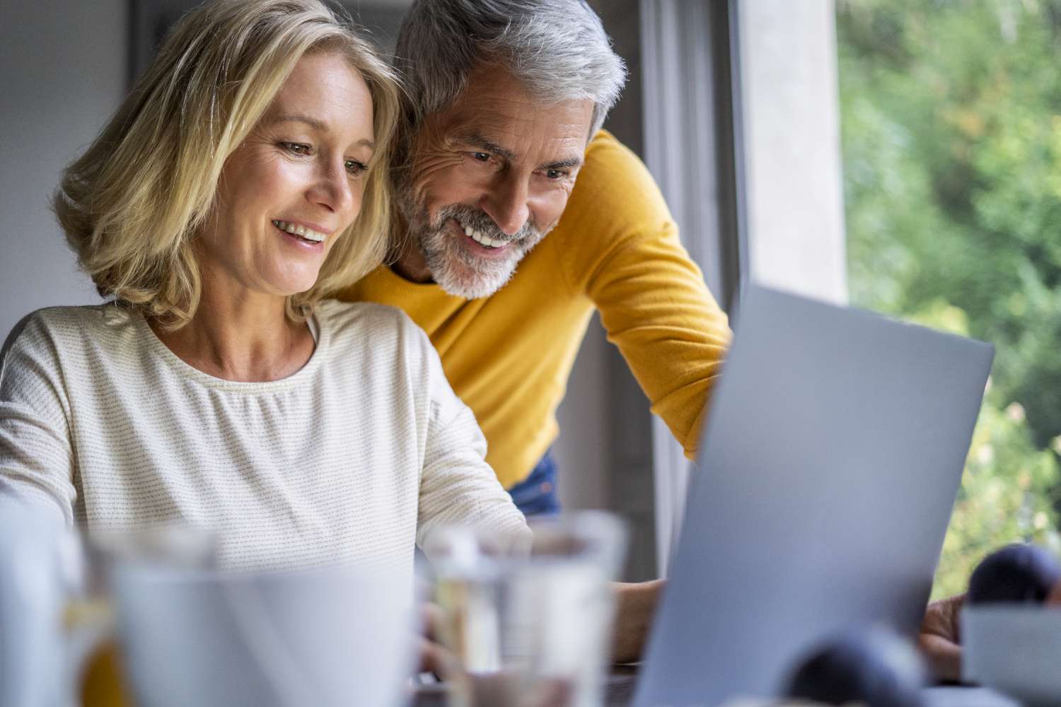 Couple in their 50s at their kitchen table looking happily at a laptop screen