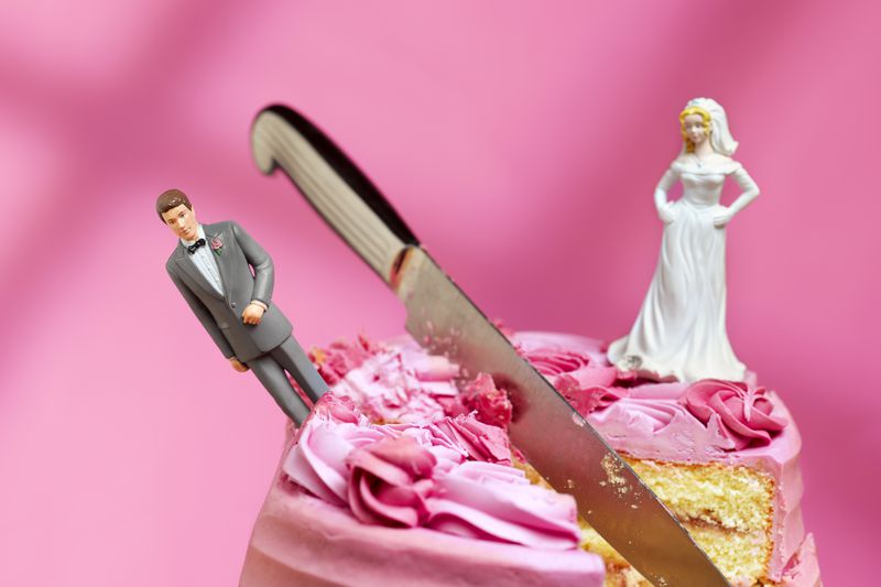 A cake with a bride and groom figurine, a knife cutting into the middle