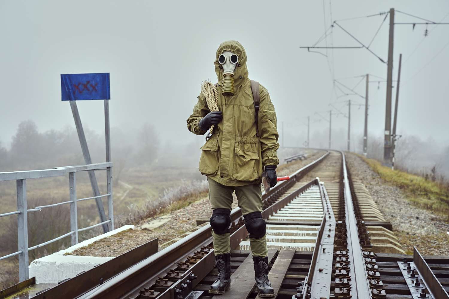 A doomsday prepper with a gas mask and rope over the shoulder on train tracks.