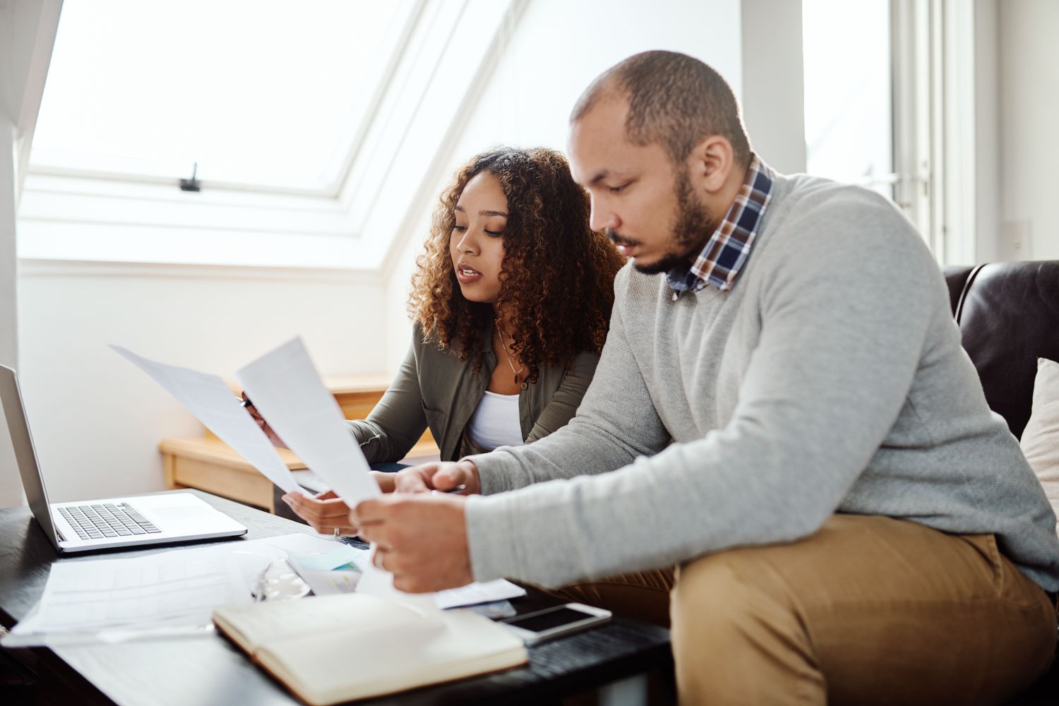 Young couple sitting on their sofa and looking together at mortgage documents and rates on a laptop