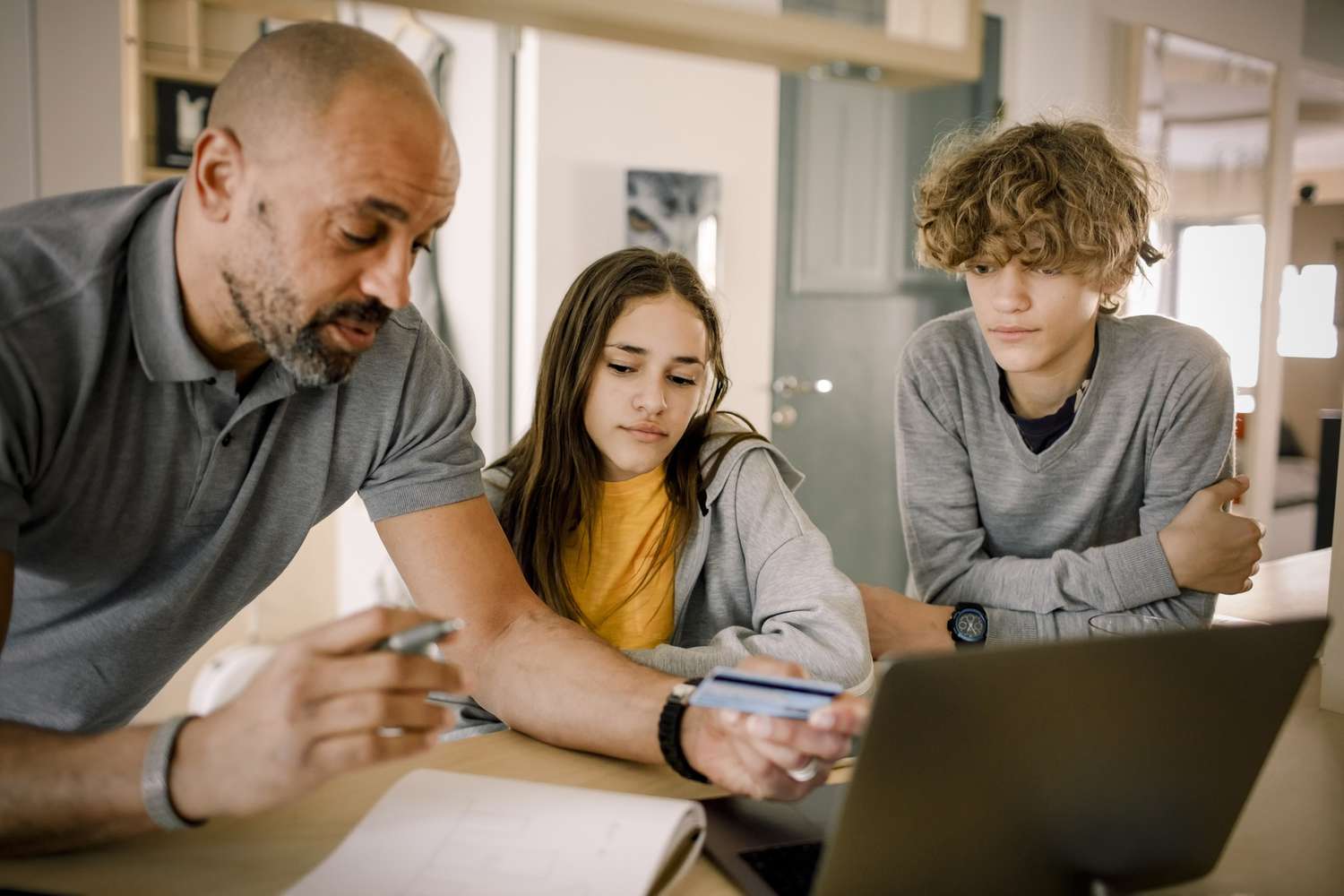 Brother and sister looking at father explaining finance with credit card