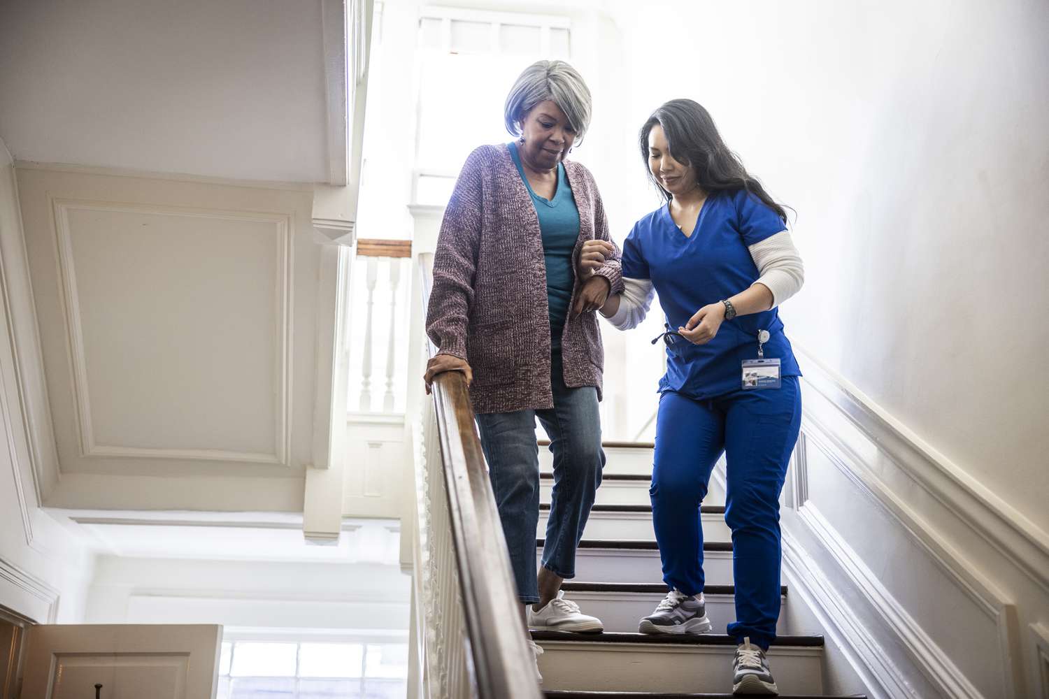 A home health aide helps a woman down the stairs