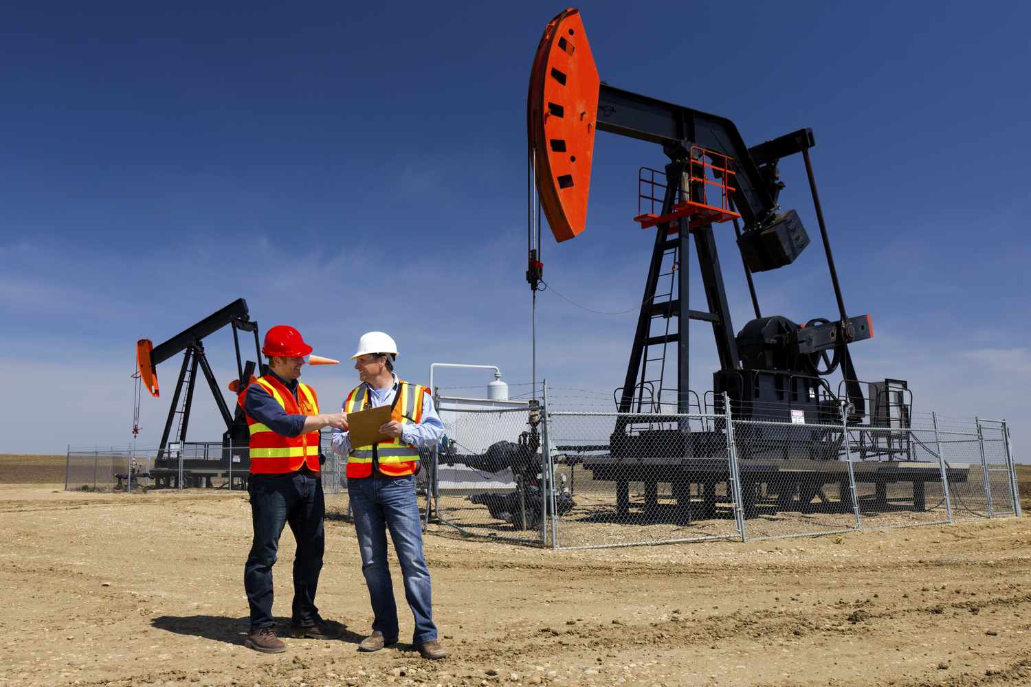 Two oil and gas workers standing in front of an oil pumpjack