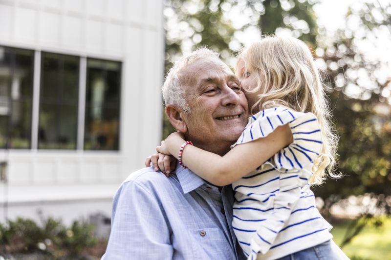 Older man holding grandchild in front of their house that is in reverse mortgage.