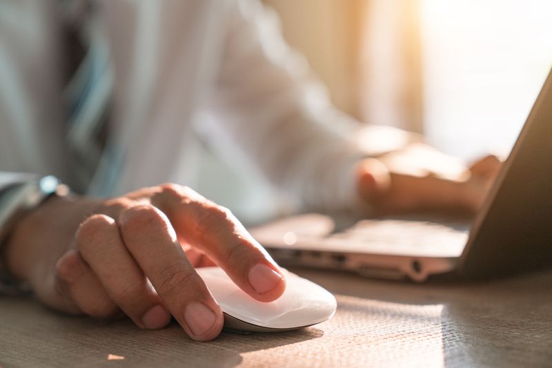 mid-section of a man clicking on a mouse and typing on a laptop
