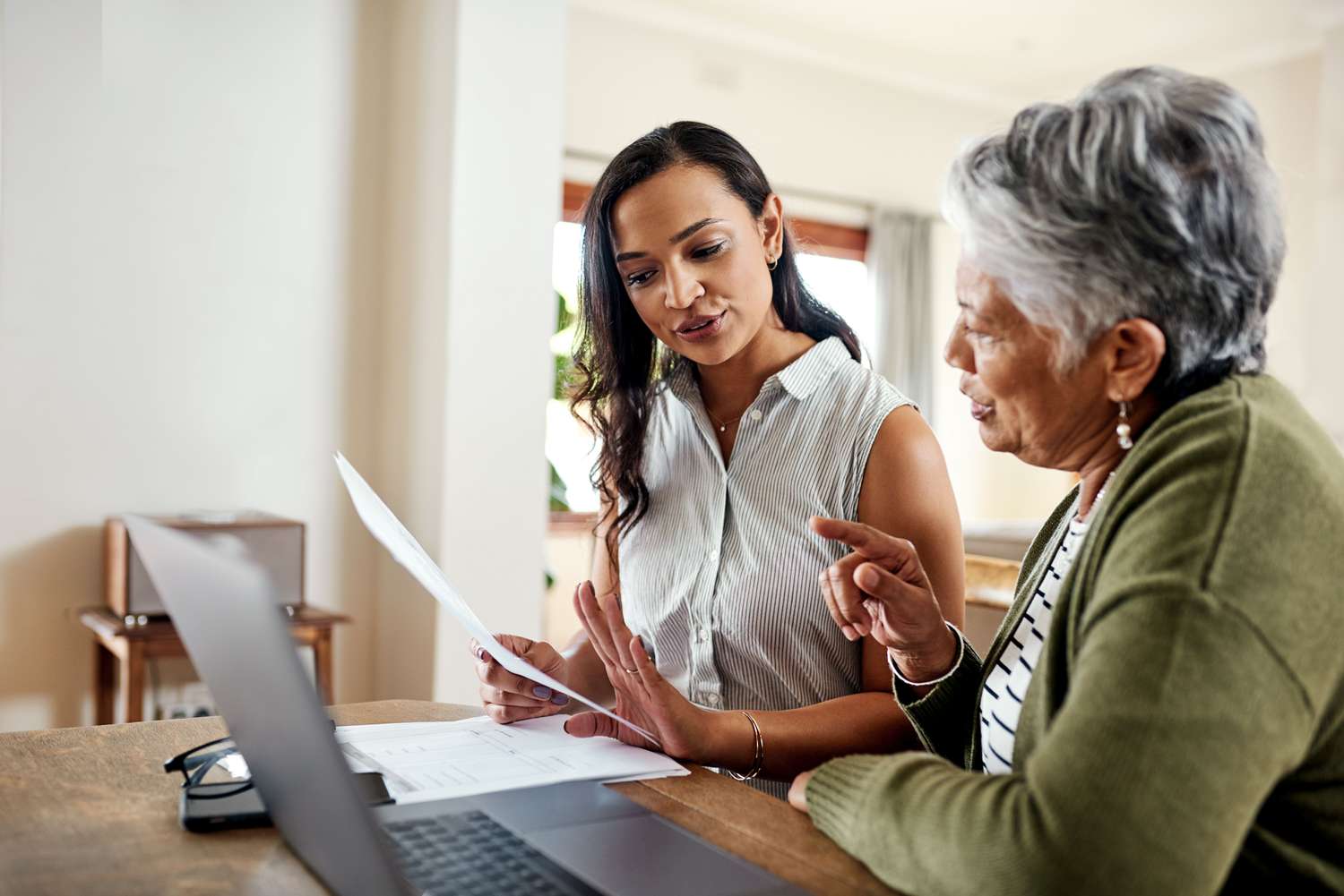 Two women discussing paperwork in front of a laptop at home