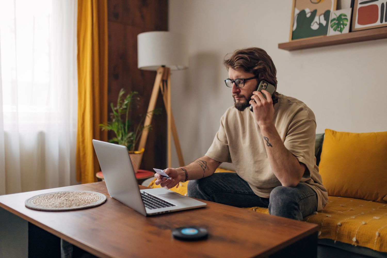 A person sitting on the sofa at home with credit card in one hand and phone in the other, trying to dispute a false credit card charge.