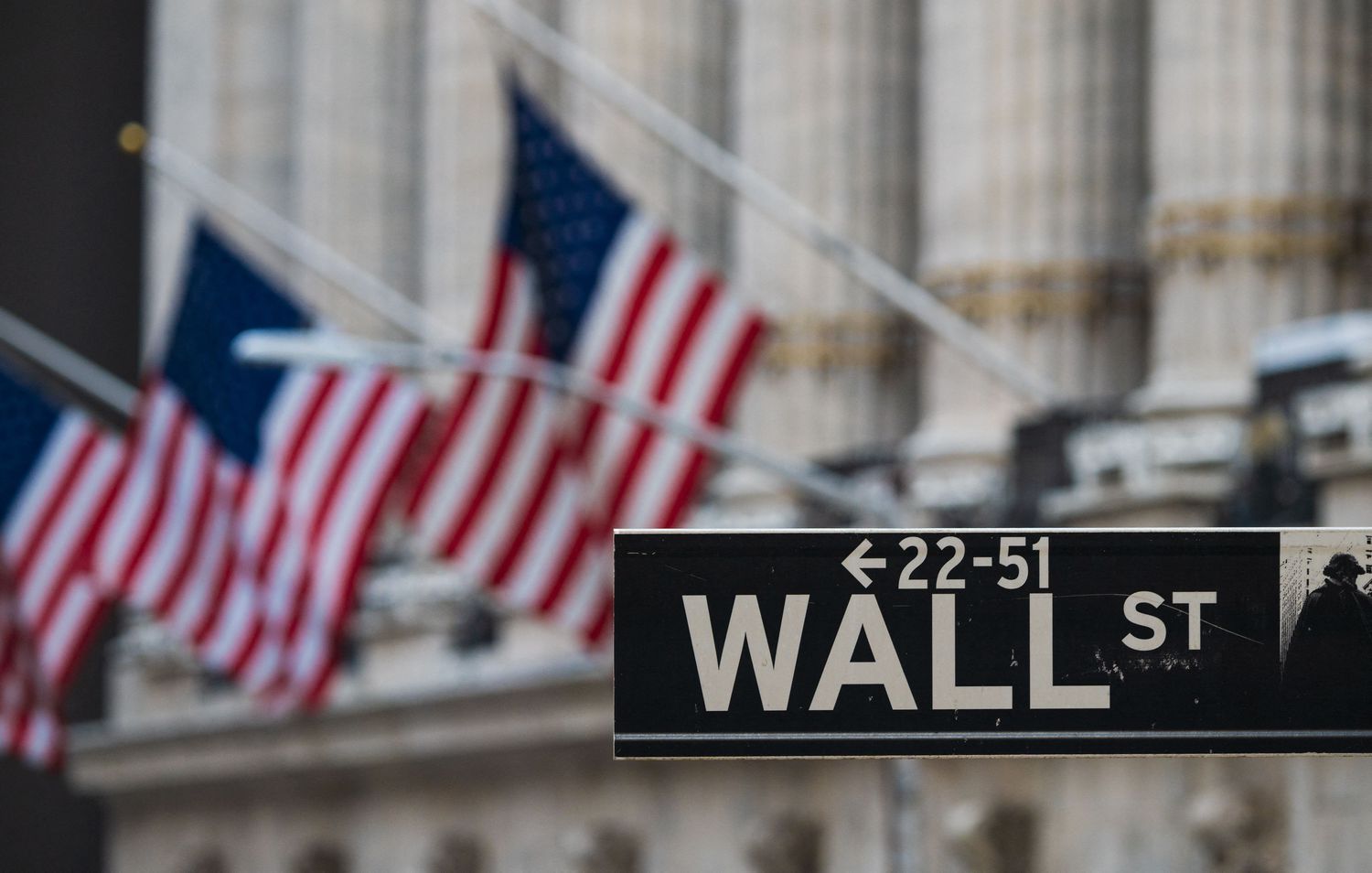 A Wall Street sign appears in front, with three American flags hanging in the background.