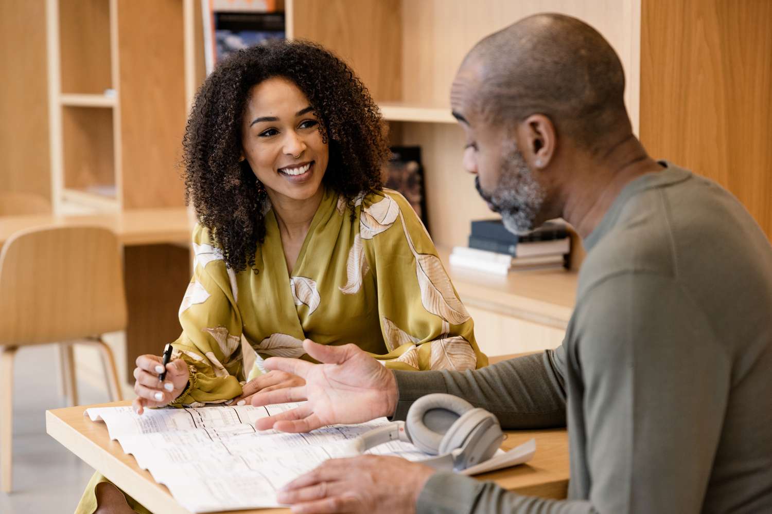 Two people at a table discussing a blueprint, one appears engaged and smiling while holding a pen