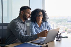 Financial advisor sitting at desk looking at laptop computer in office with client
