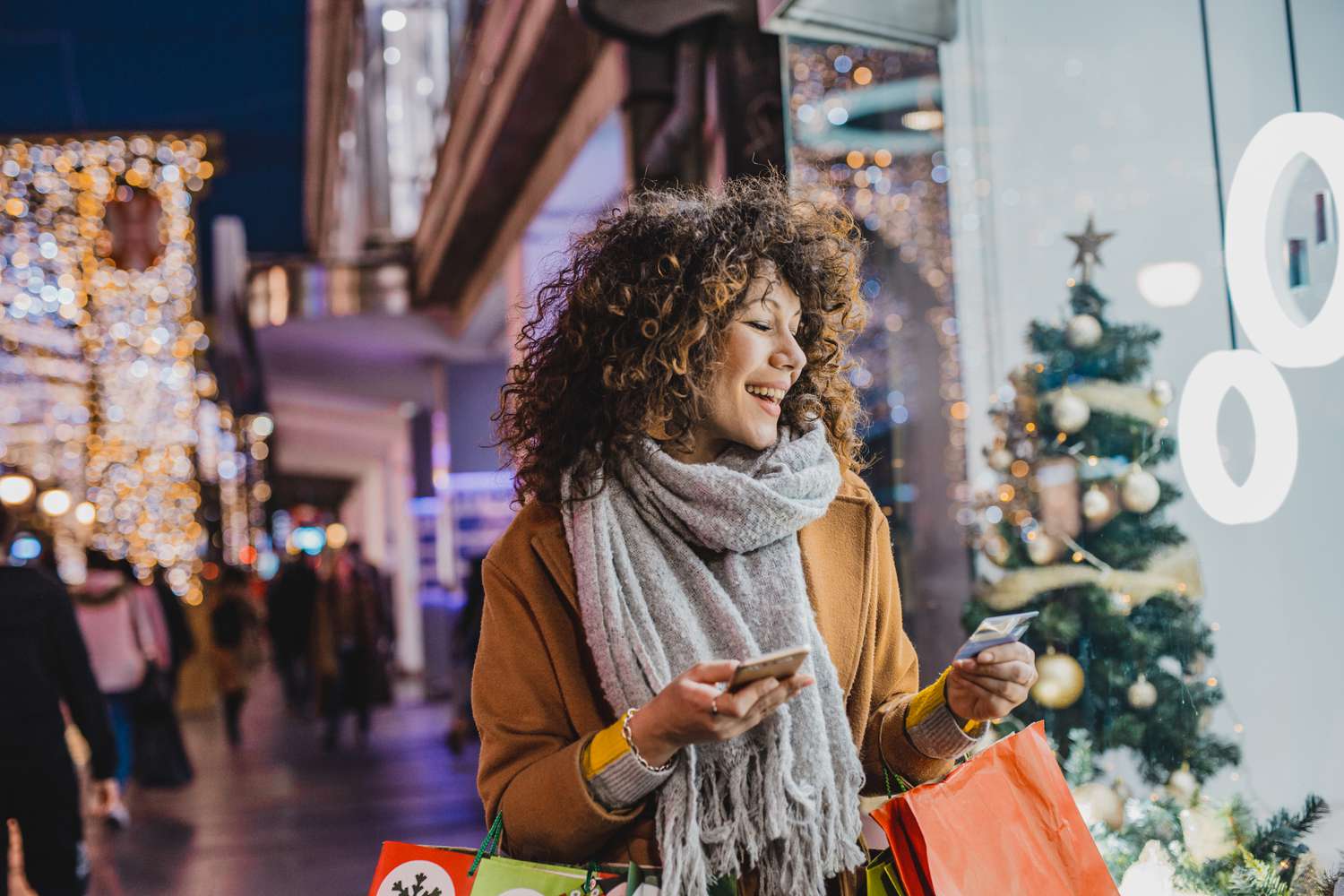 Young woman standing with Christmas presents outdoors, holding smart phone and a credit card
