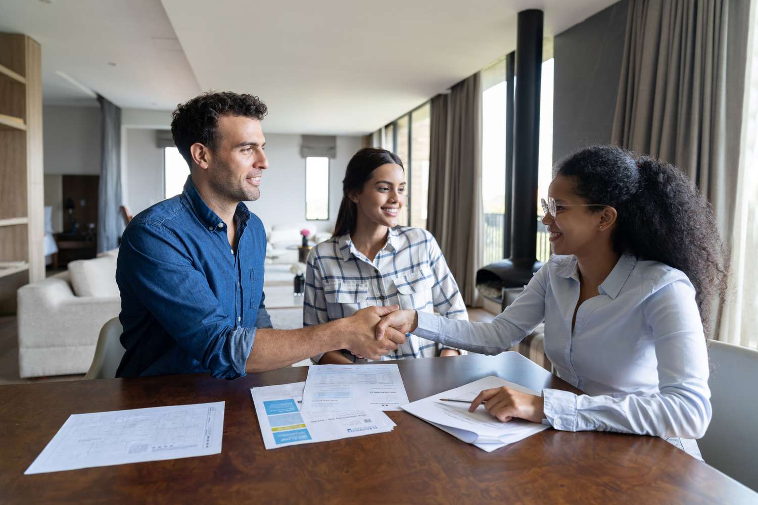 A young adult couple shake hands with a loan officer after completing mortgage loan pre-qualification paperwork.