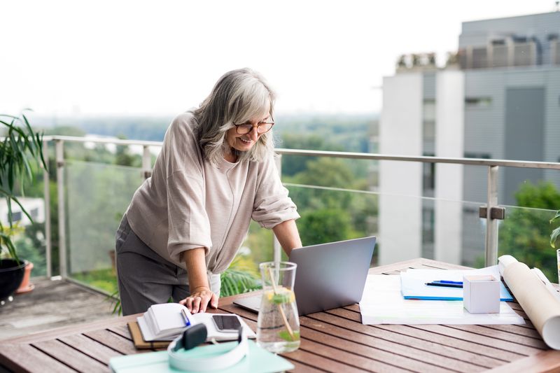 A woman uses a laptop on an outdoor table surrounded by work materials, overlooking an urban setting.
