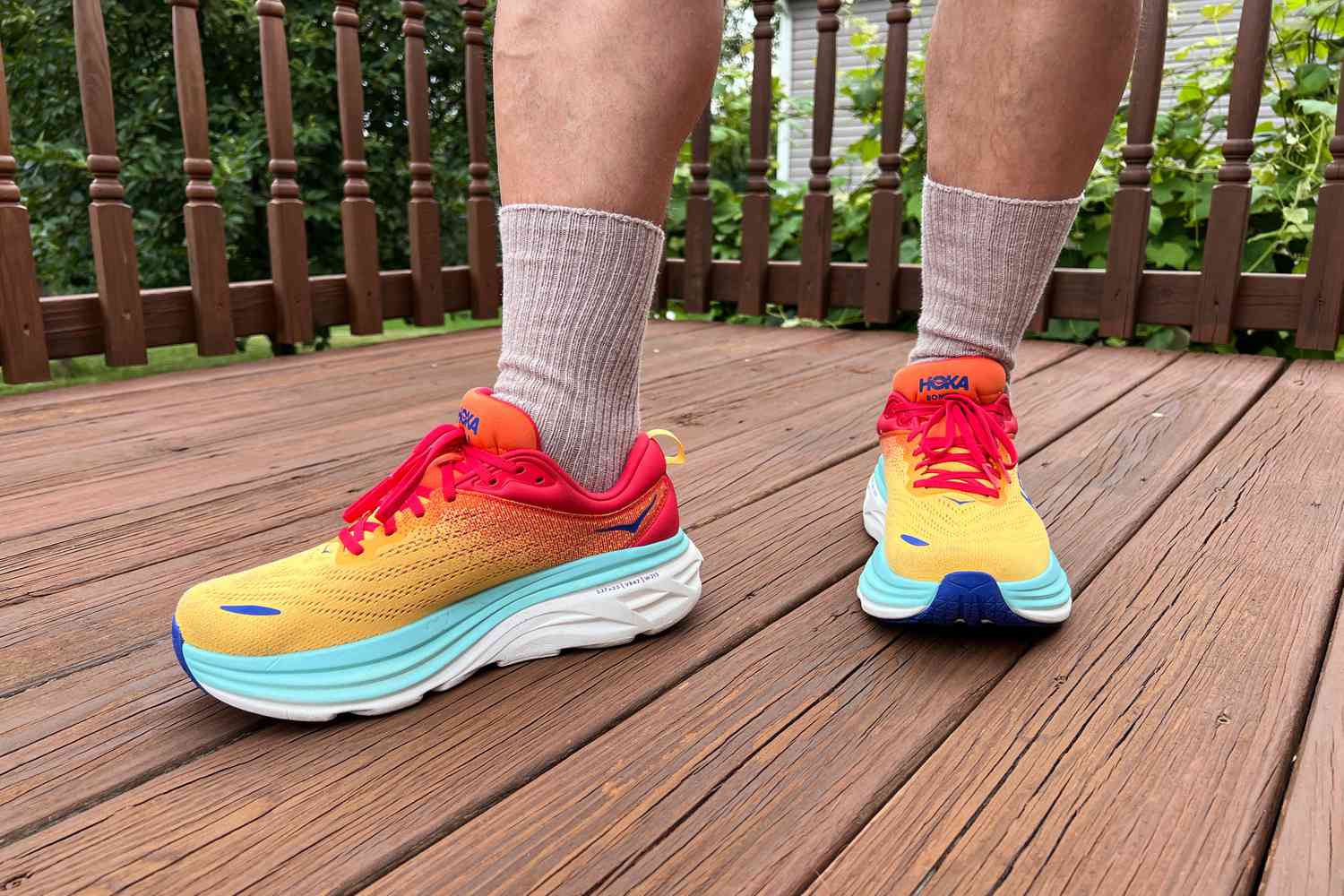 A person stands outside on a deck wearing the Hoka Men's Bondi 8 Everyday Running Shoes
