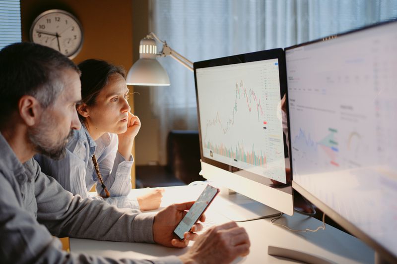 A couple looking charts and other financial data on two computer monitors 