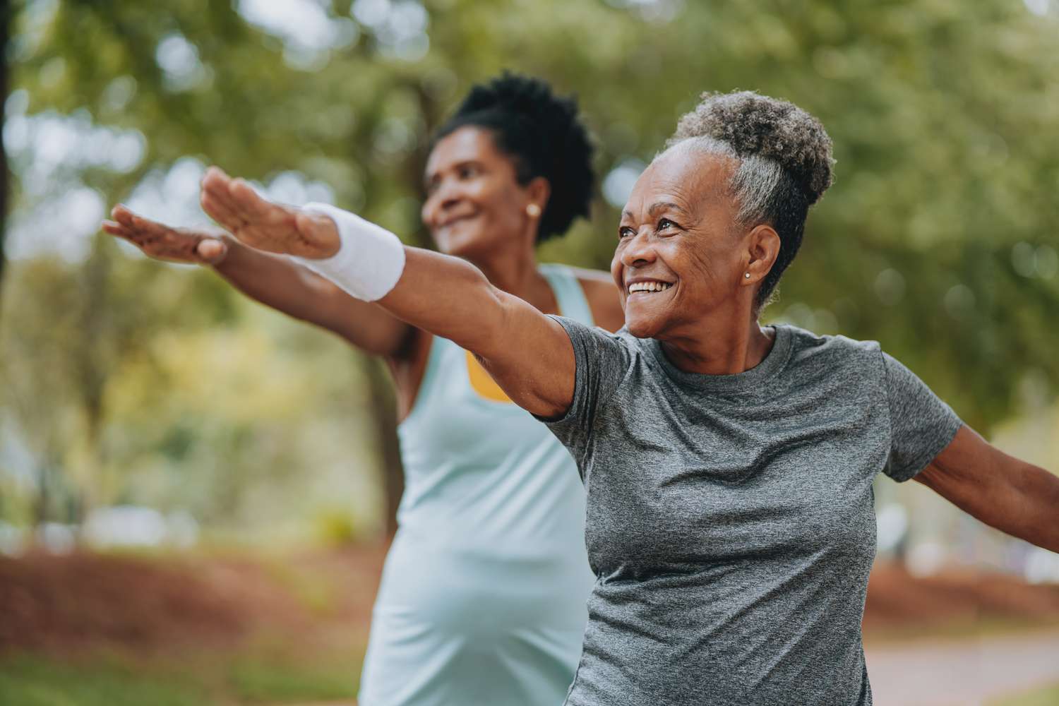 Two senior women exercising together outside. 