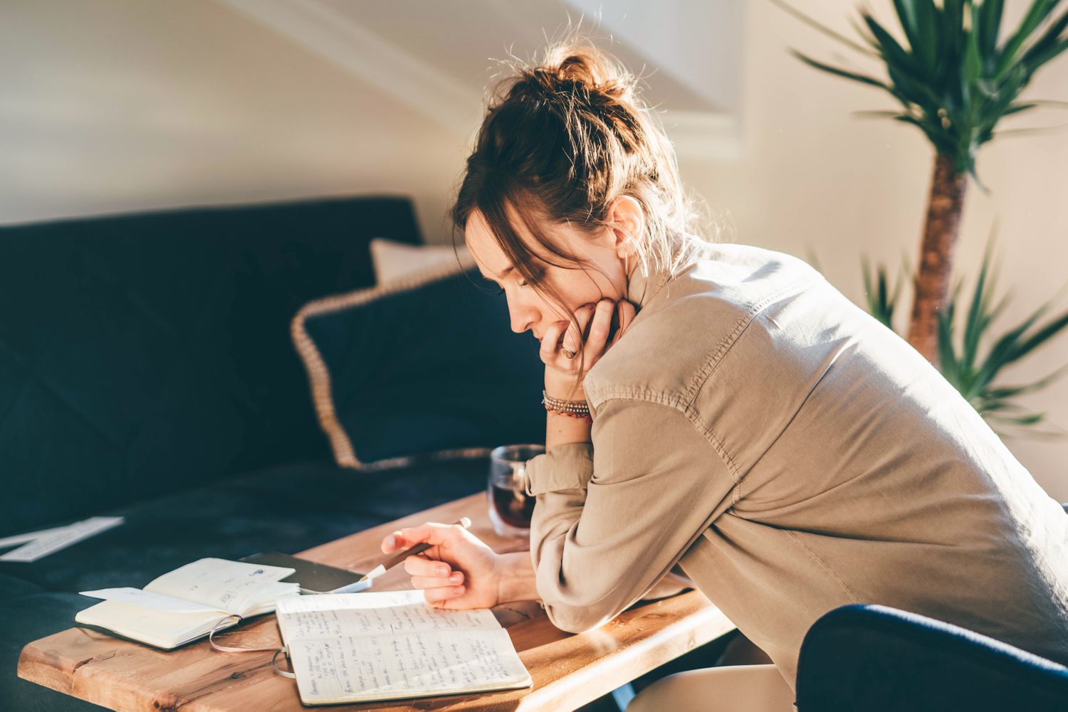 A woman leans over a table in a living room, writing in a journal. 