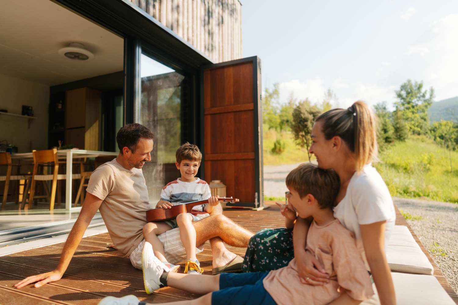 family listening to child playing guitar on front deck of vacation house